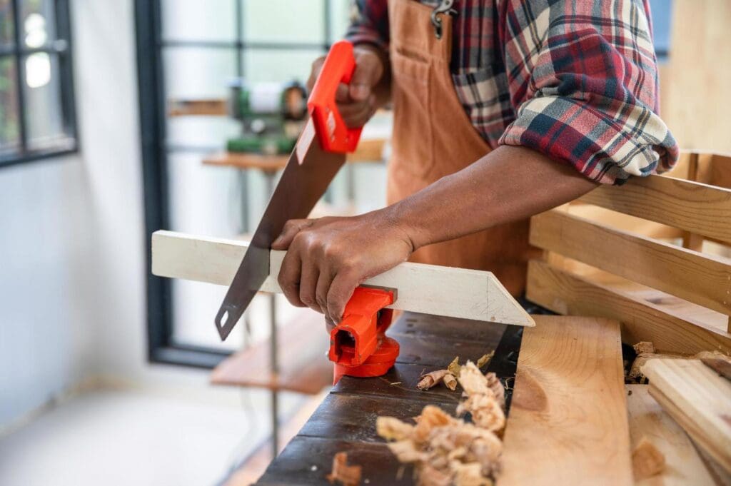 Carpenter sawing wood with hand saw.