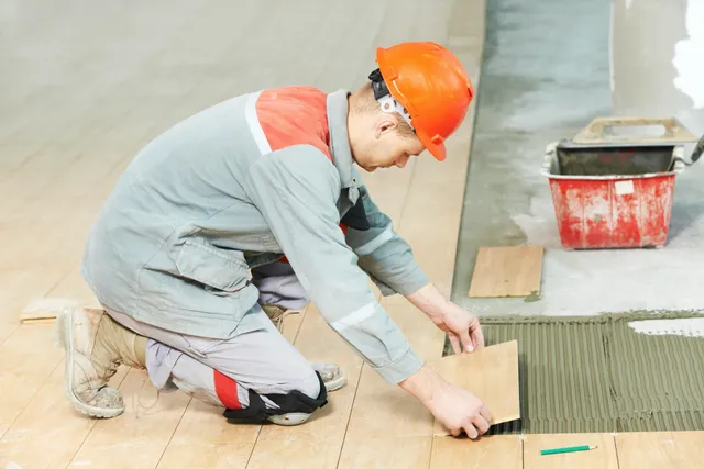 Worker installing wood flooring tiles.