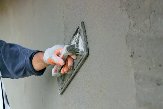 Here's an alt tag for the image: Hand applying plaster to wall.