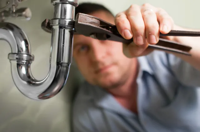 Plumber fixing sink pipe with pliers.